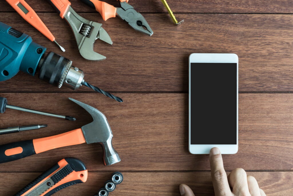 A hand touching a smartphone with tools to the side on a wooden background